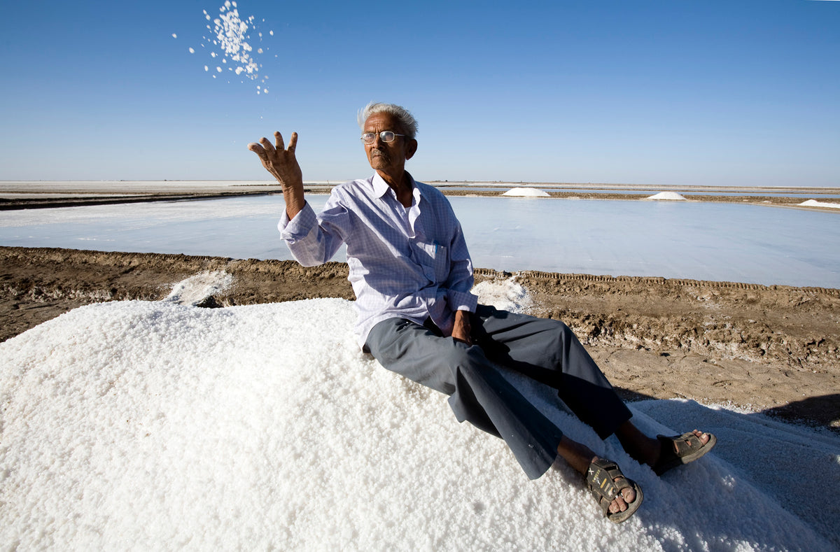 farmer sitting on a pile of surya salt and throwing some in the air in the salt district of Gujarat