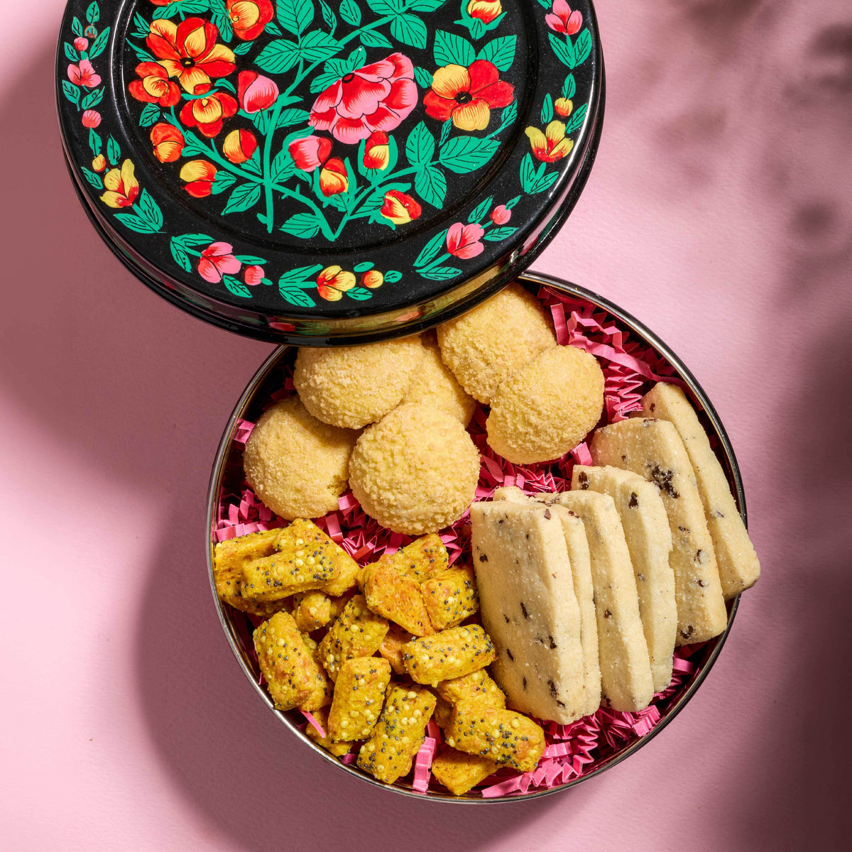 Open tin filled with various cookies on a pink background