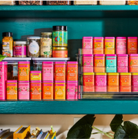 Colorful Diaspora Co. spice tins arranged in rows on a teal shelf, with assorted jars and containers.